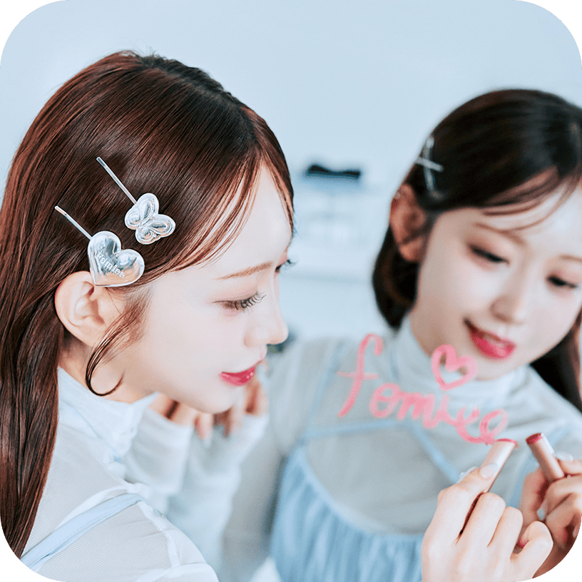 女性が鏡にリップでハート付きの「femiee」と書き、髪には蝶とハートのヘアピンを着けているシーン